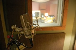 The microphone in the vocal booth at Silver Star Recording music studio is illuminated by light from a lamp. The studio's control room is on the other side of the window.